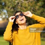 Portrait of cheerful young asian woman holding sunglasses and laughing outside